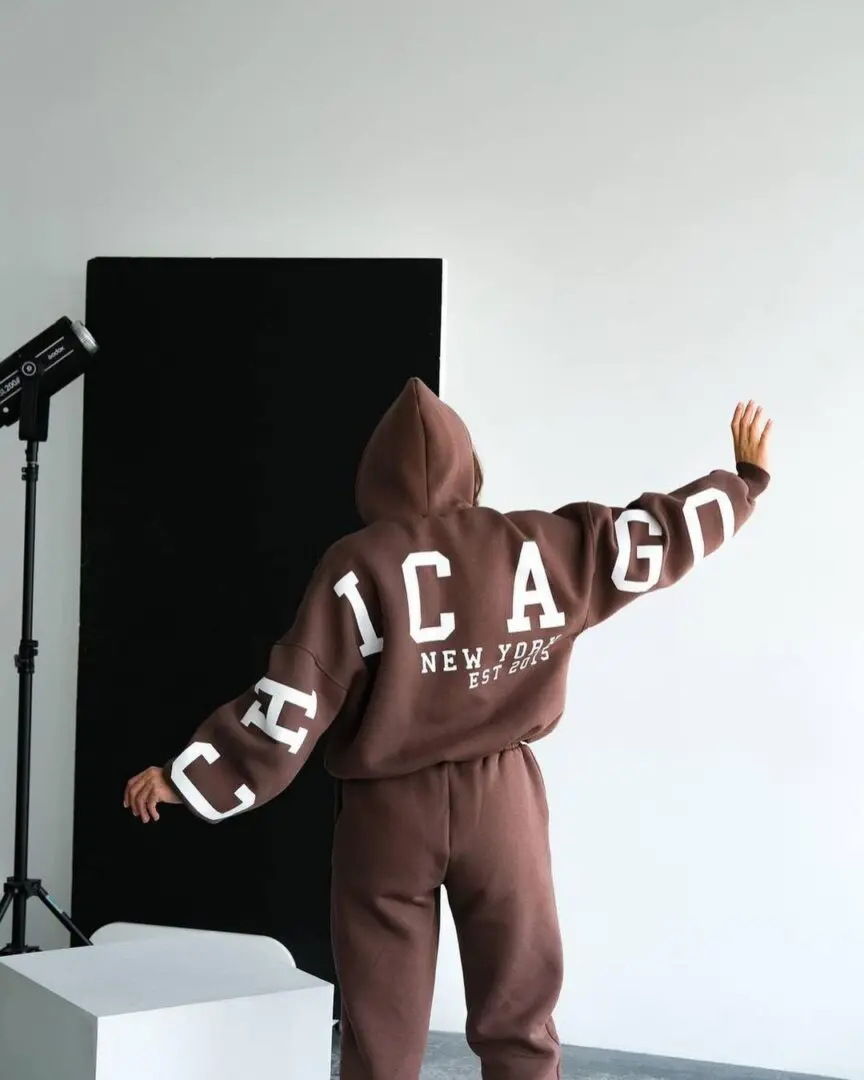 A person in a brown hoodie standing next to a white wall.