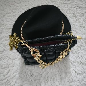 A black purse with gold chain and a hat on top of it.