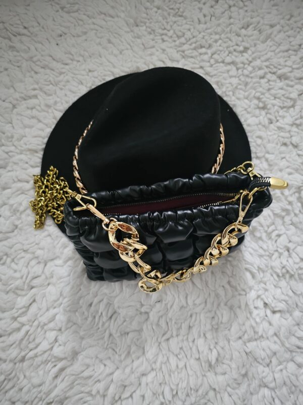 A black purse with gold chain and a hat on top of it.